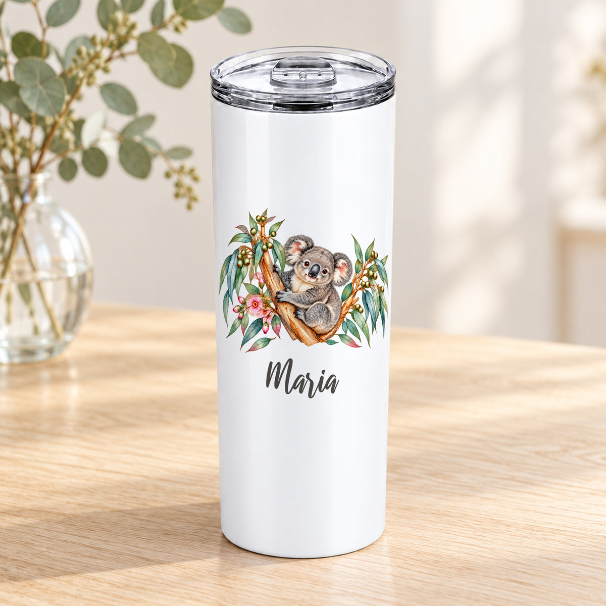 Weißer Thermobecher mit Koala-Aquarellmotiv und Wunschname auf einem Holztisch mit Eukalyptus.