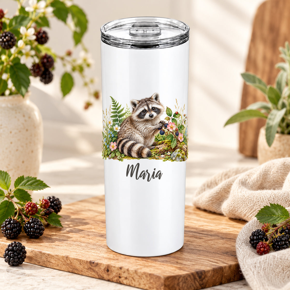 Weißer Thermobecher mit Waschbär-Aquarellmotiv und Wunschname auf einem Holzbrett neben Beerenzweigen.