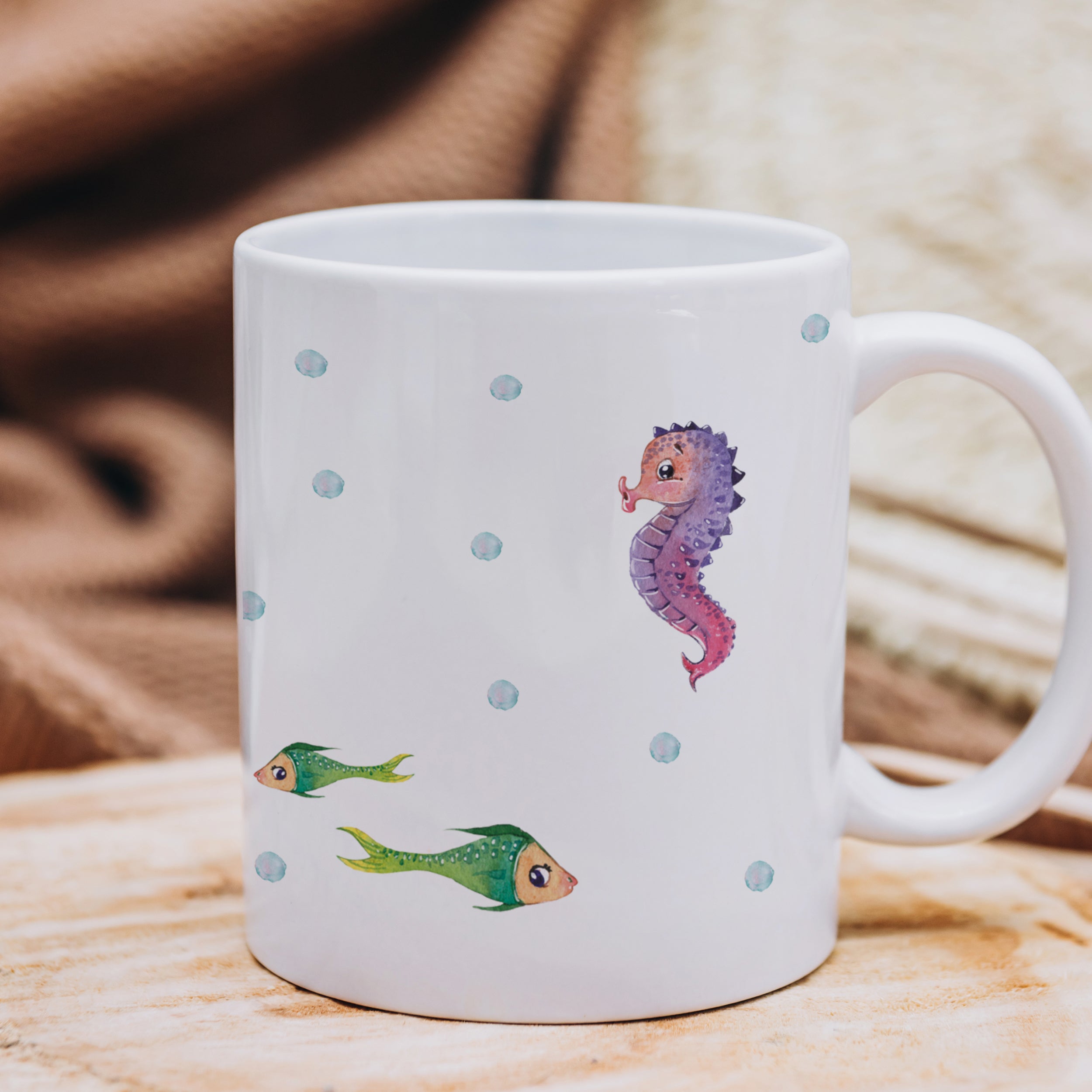Weißer Becher mit bunten Seepferdchen und Fischen.