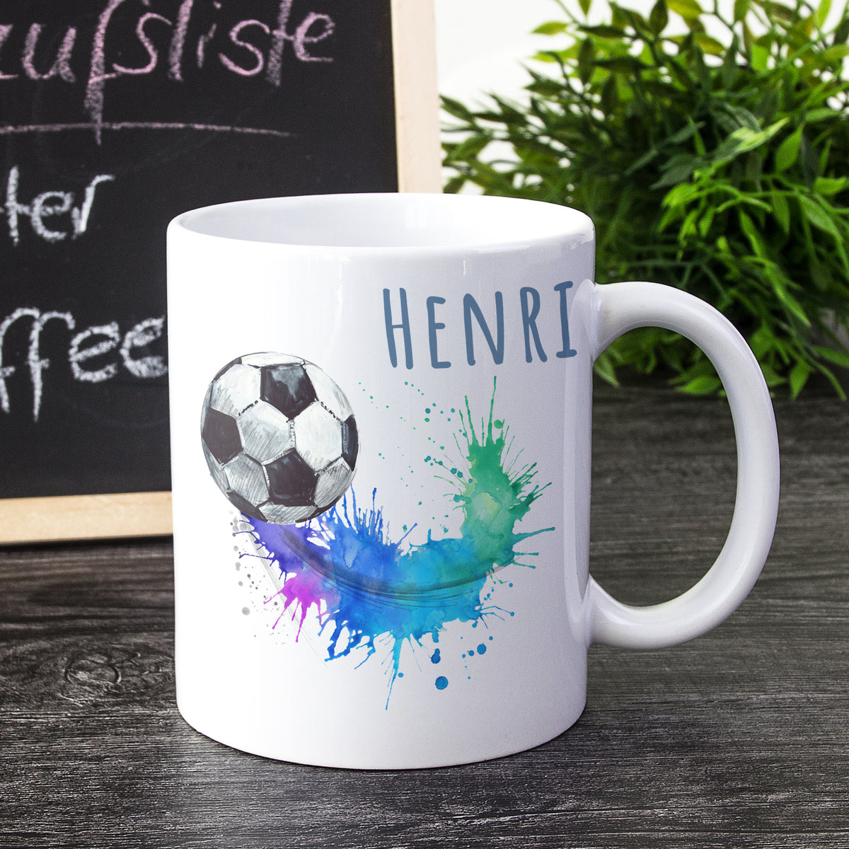 Weißer Kaffeebecher mit Fußball und buntem Spritzdesign.