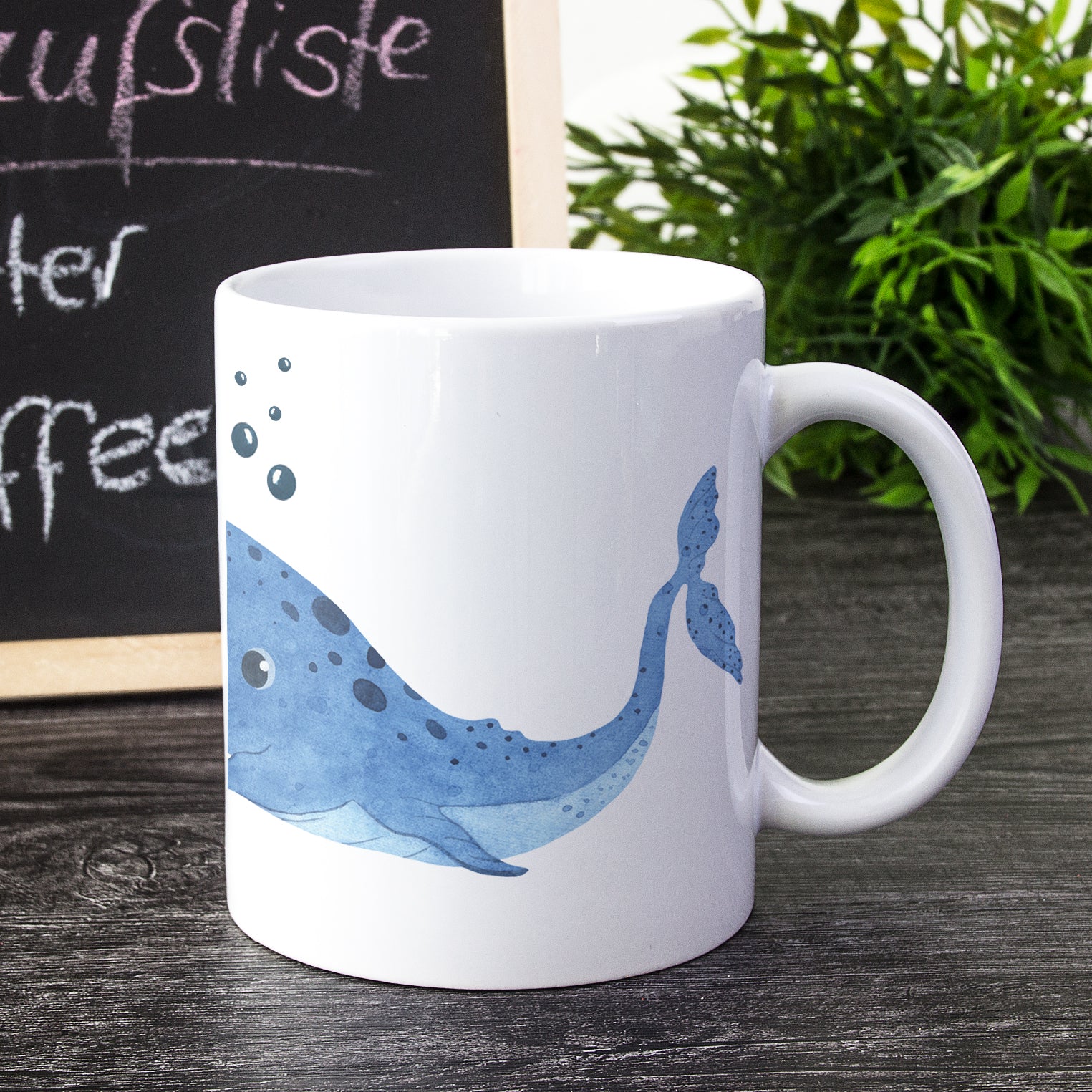 Weißer Becher mit blauem Wal-Motiv und Blasen.