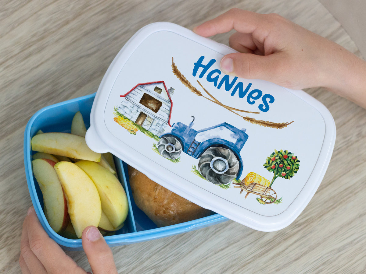 Blaue Brotdose mit Traktor-Motiv und Äpfeln.