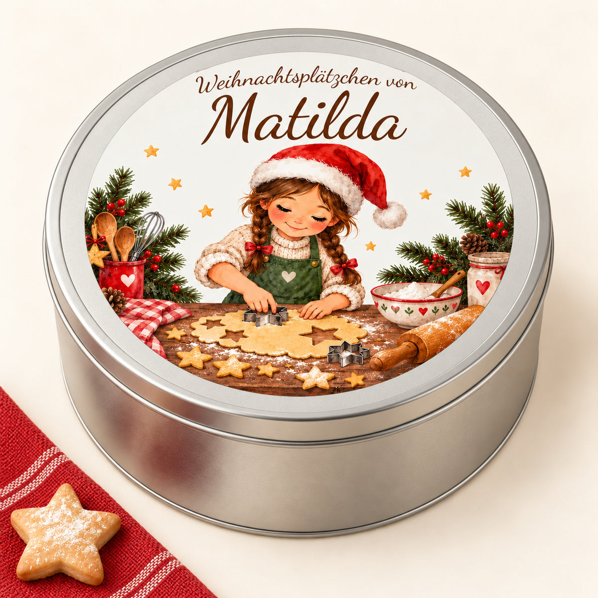Silberne Keksdose schräg von oben mit Weihnachtsbäckerin, Wunschname und Sternplätzchen neben rotem Tuch.