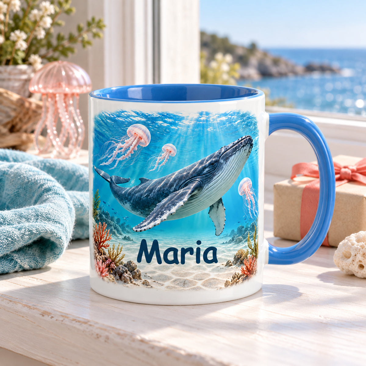 Wal-Tasse im Quallengarten mit Name Maria auf einer Fensterbank mit Meerblick, Tuch und Buch