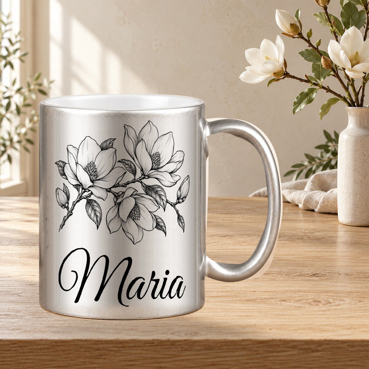 Silberne Tasse mit schwarzem Magnolienmotiv und Wunschnamen in einer dekorierten Blumenszene.