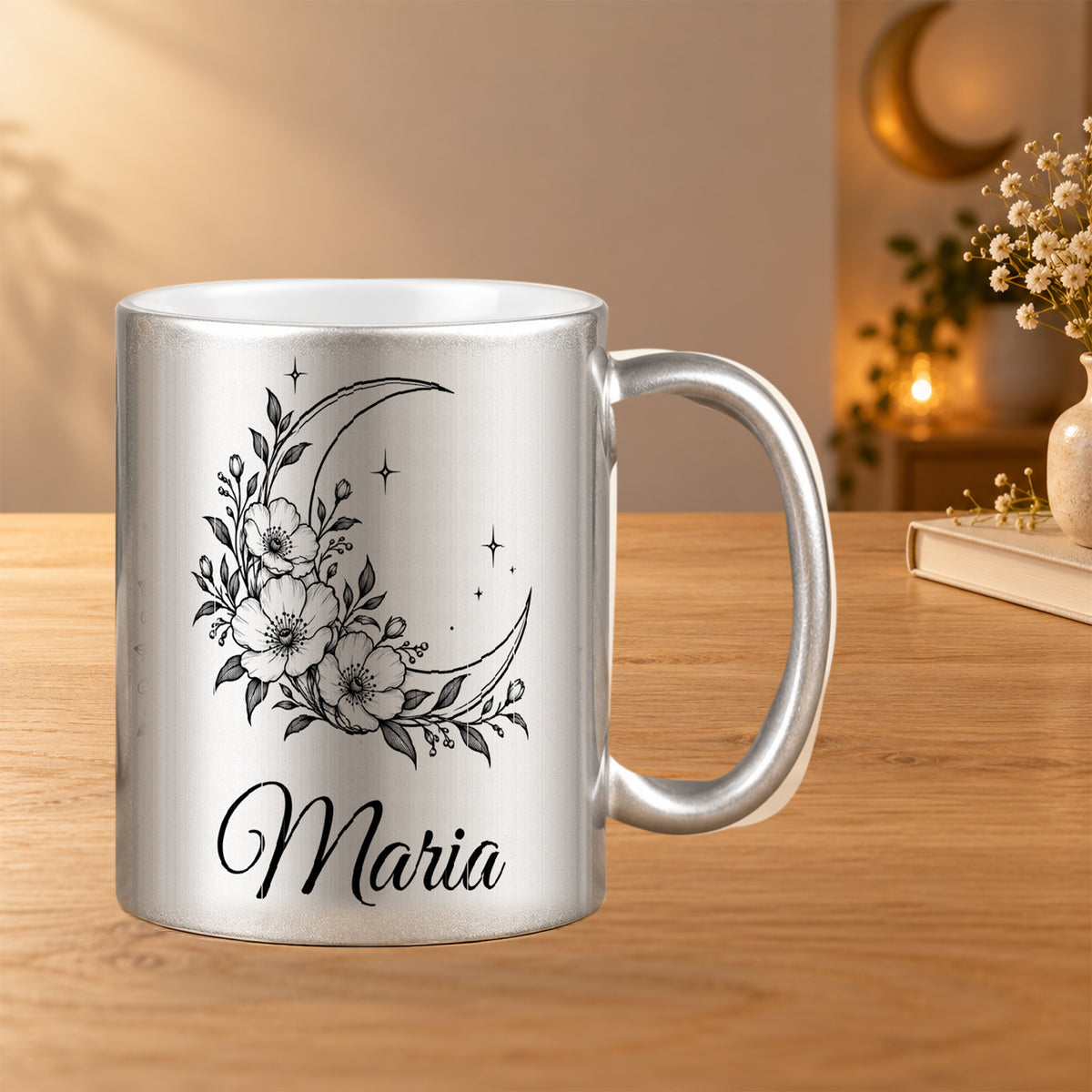 Silberne Tasse mit schwarzem Mond-Blumenmotiv und Wunschnamen in einer warmen Tischszene mit Monddekoration.