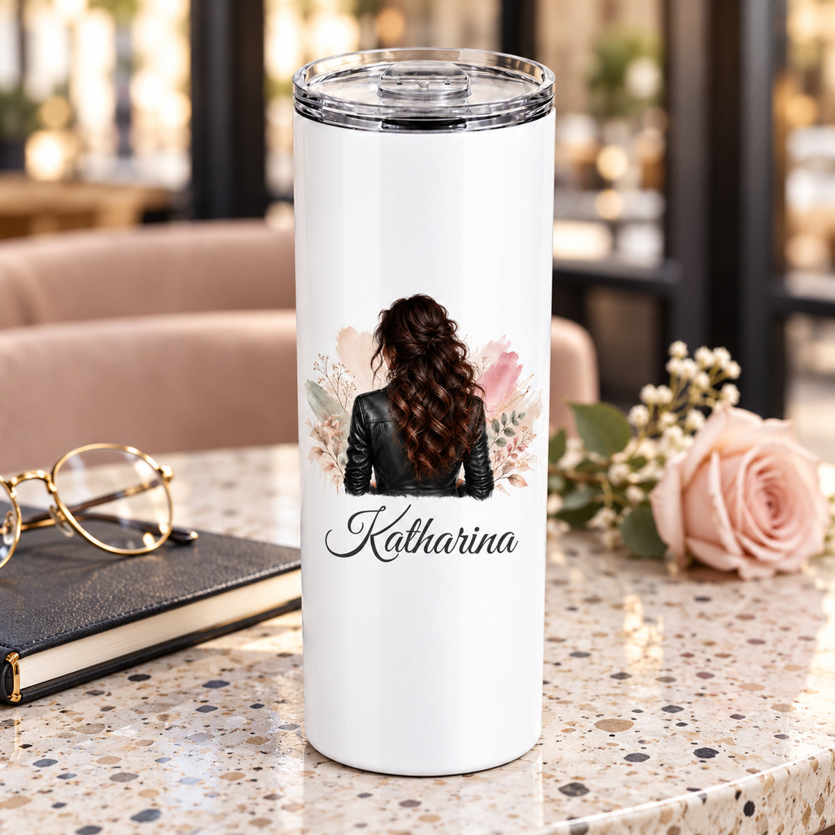 Thermobecher mit Namen und Frauenmotiv mit dunklen Naturlocken und schwarzer Lederjacke in einer Cafészene.