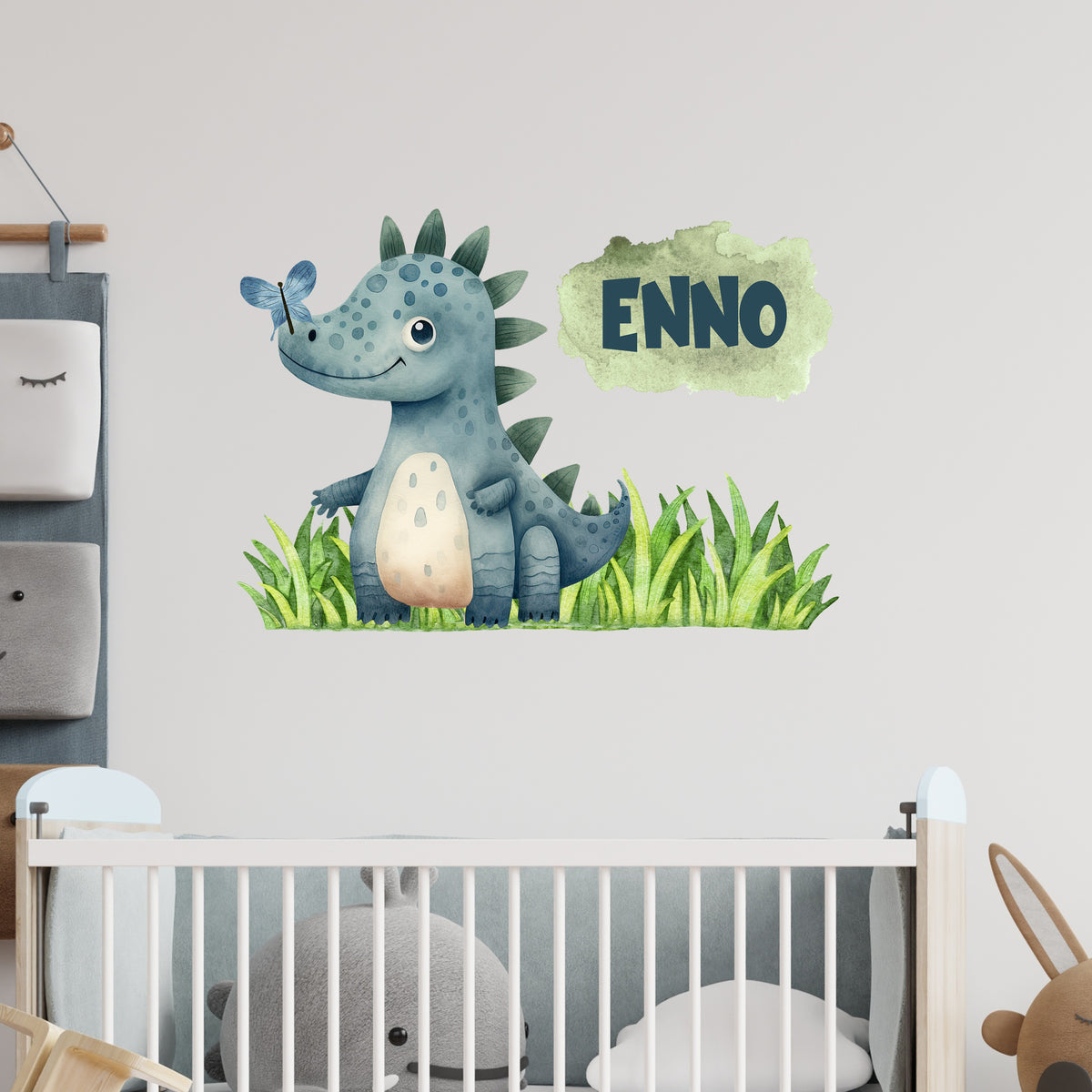 Wandtattoo mit blauem Dinosaurier, Gras und Wunschname über Kinderbett