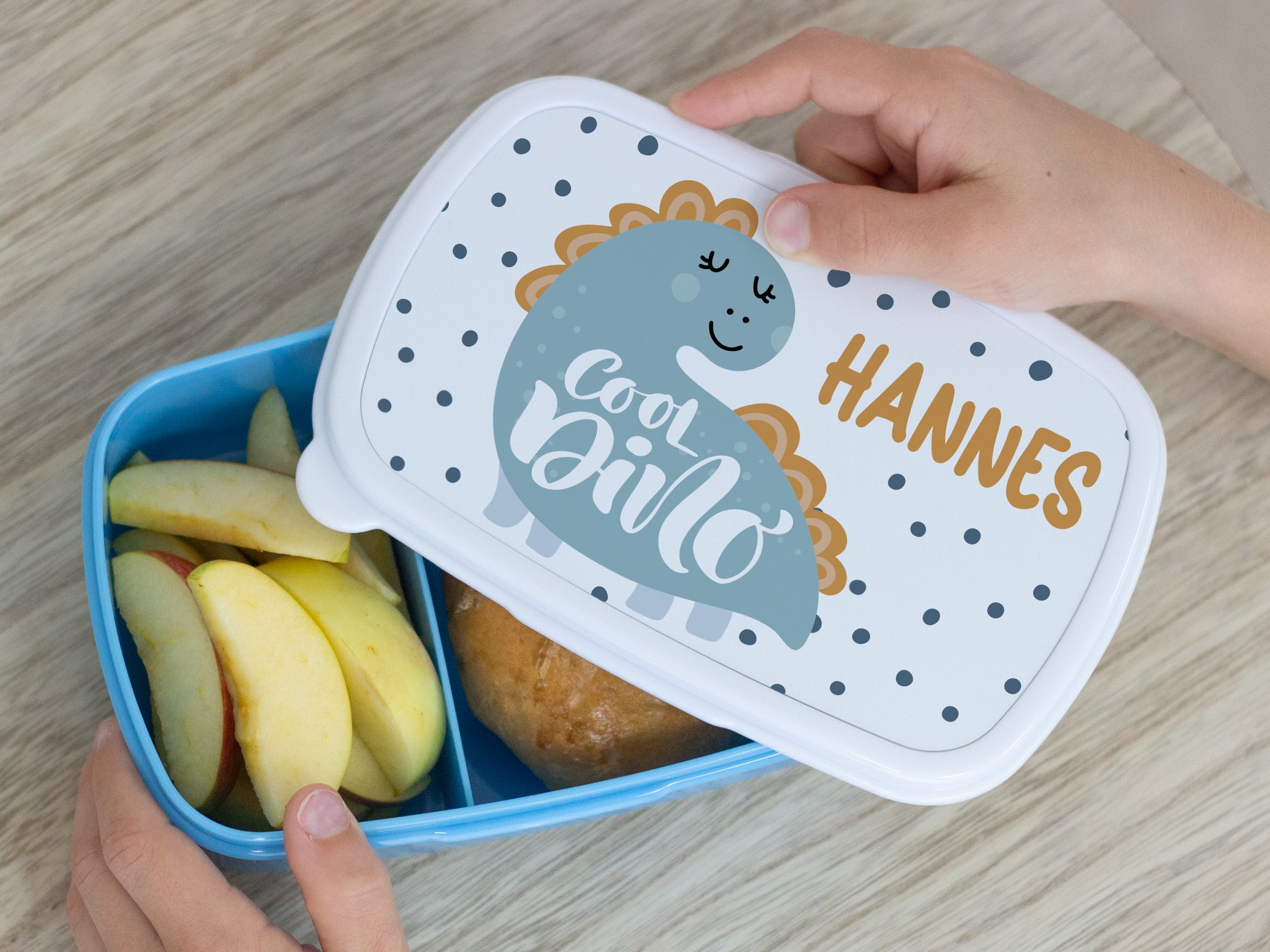 Bento-Box in Blau mit Dinosaurier-Design und Äpfeln.