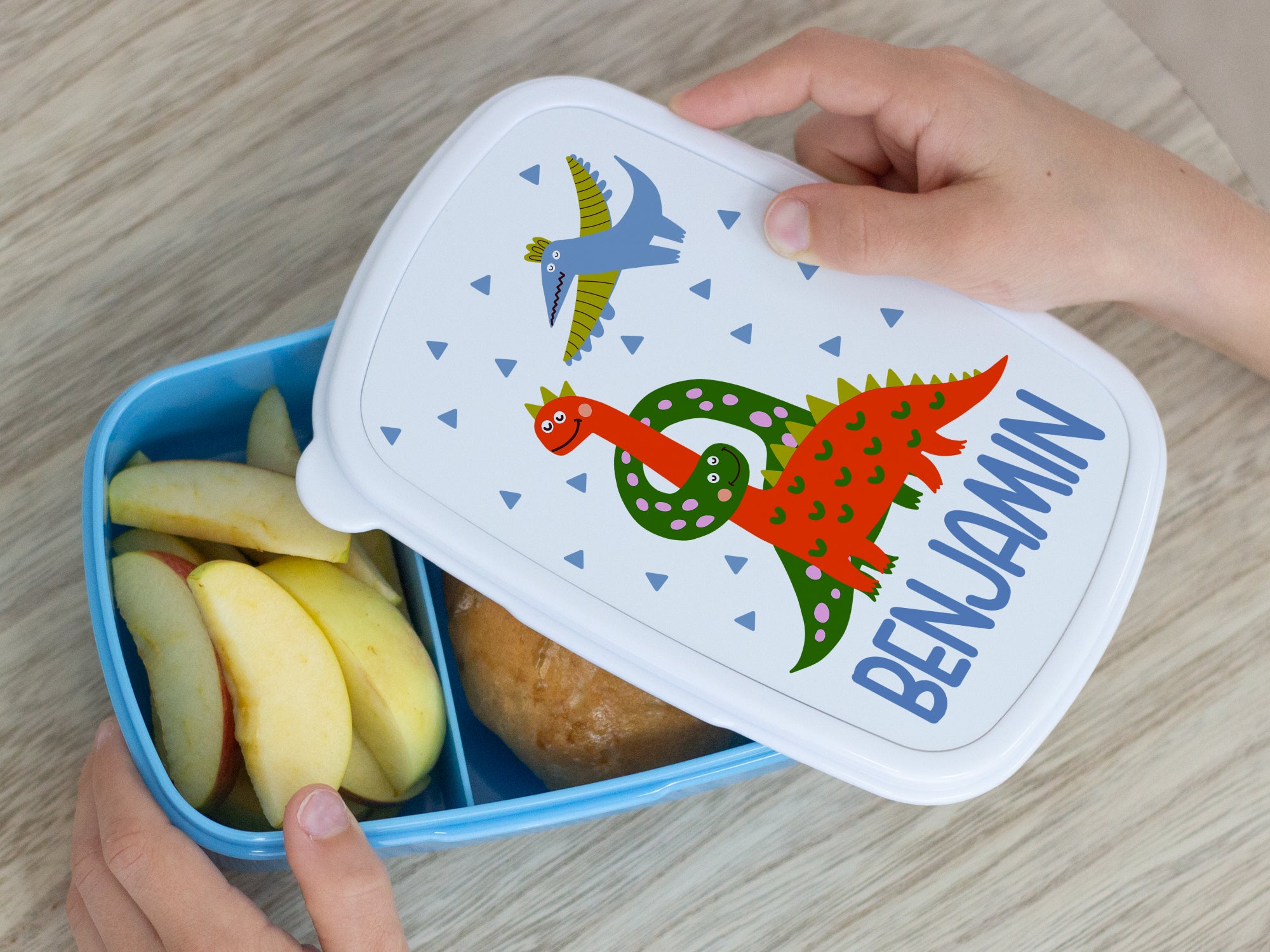 Bunte Brotdose mit Dinosaurier-Motiv und Äpfeln.