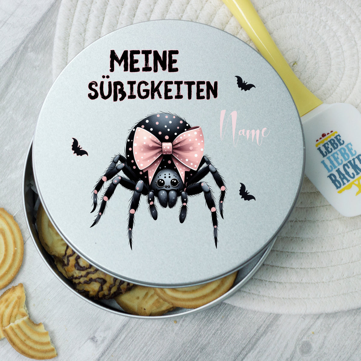 Silberne Dose mit schwarzer Spinne und rosa Schleife.