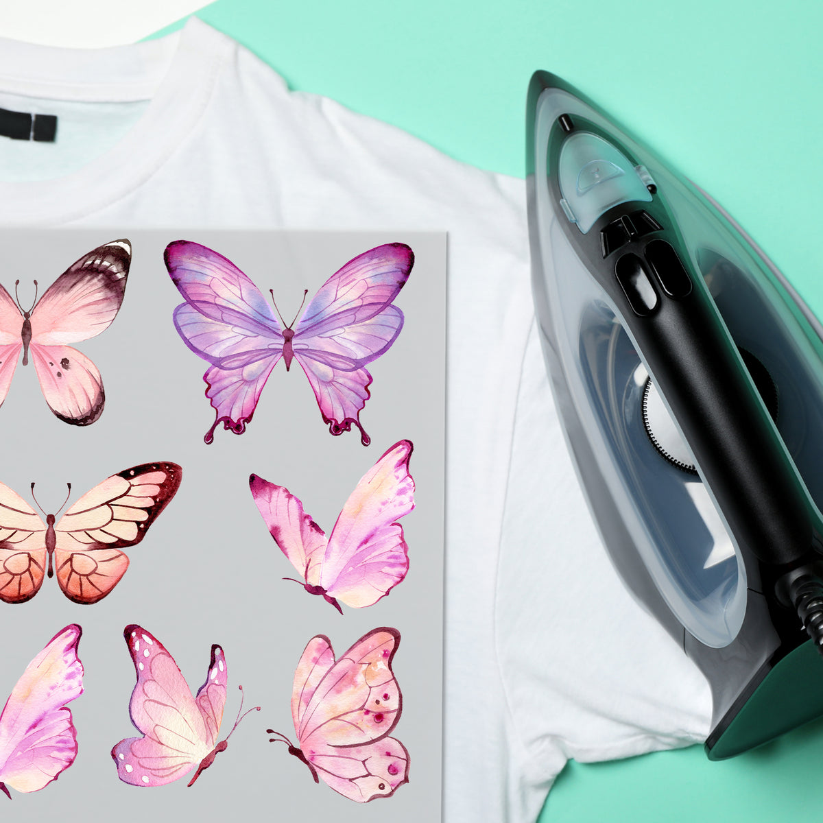 Weißes T-Shirt mit rosa Schmetterlingen und Bügeleisen.