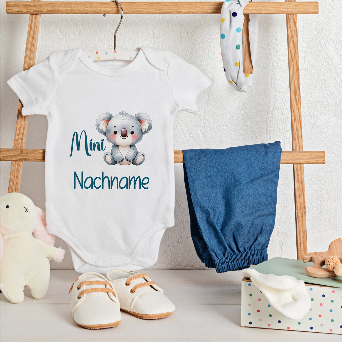 Weißes Baby-Body mit Koala-Motiv und blauem Hosenrock.