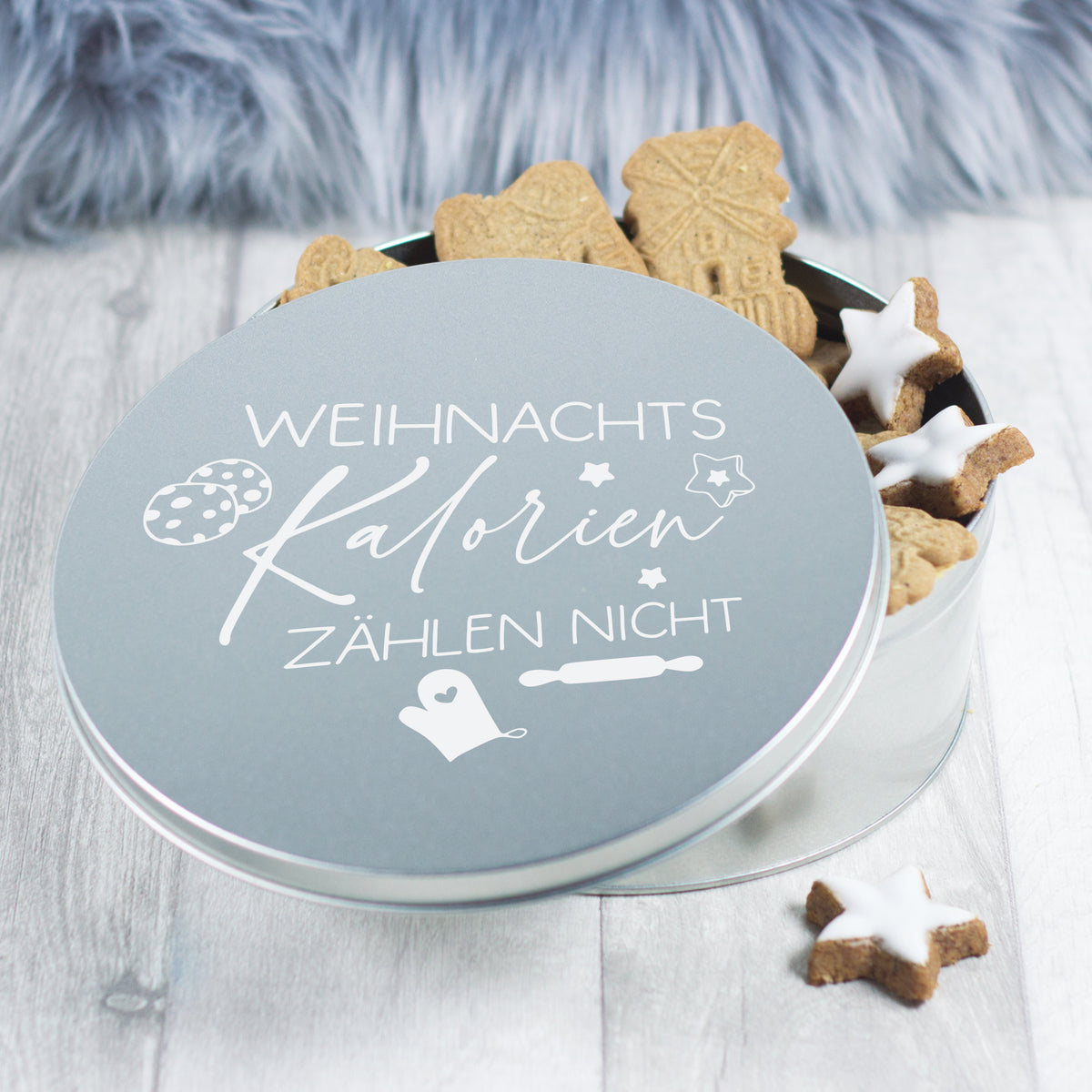 Runde, graue Keksdose mit Weihnachtsmotiv und Plätzchen.
