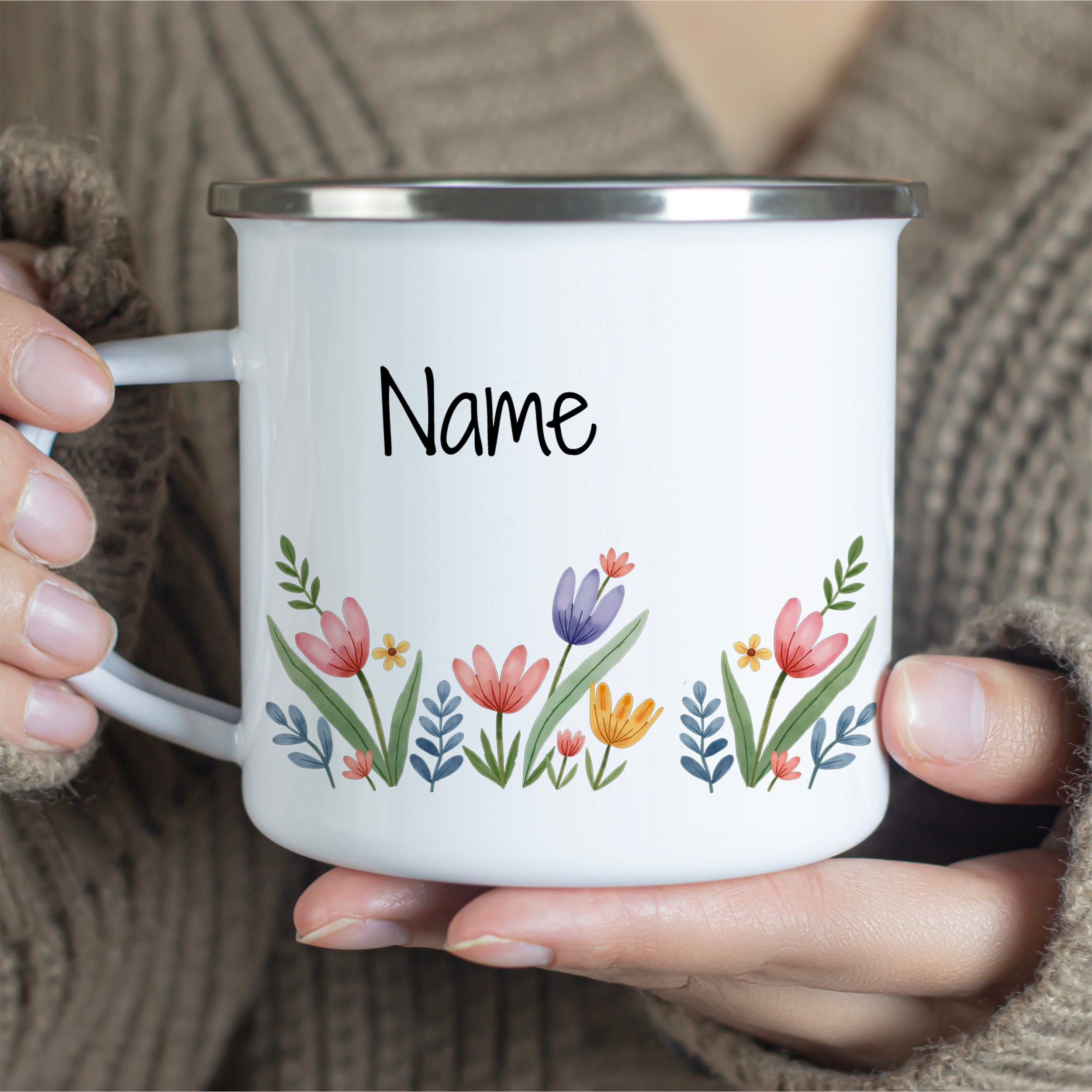 Weißer Emaillebecher mit bunten Blumen und personalisiertem Namen.