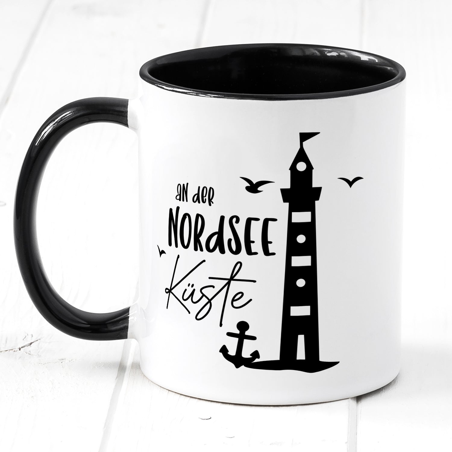 Schwarze Tasse mit Leuchtturm und Nordsee-Küstenmotiv.