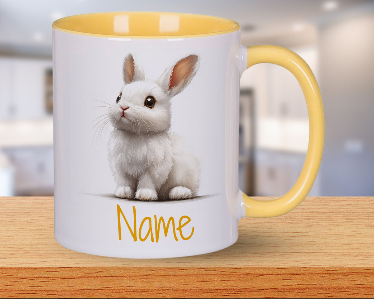 Weißer Kaffeebecher mit gelbem Henkel und Kaninchenmotiv.