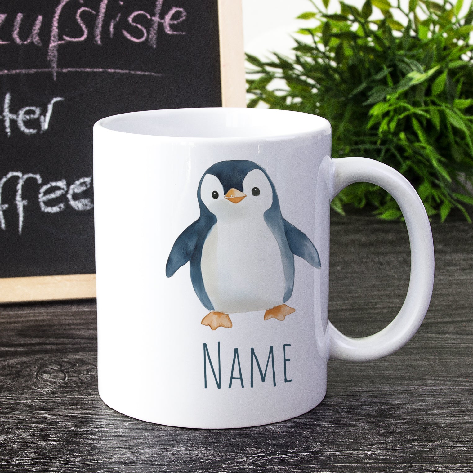 Weißer Kaffeebecher mit Pinguin-Motiv und Platz für Namen.