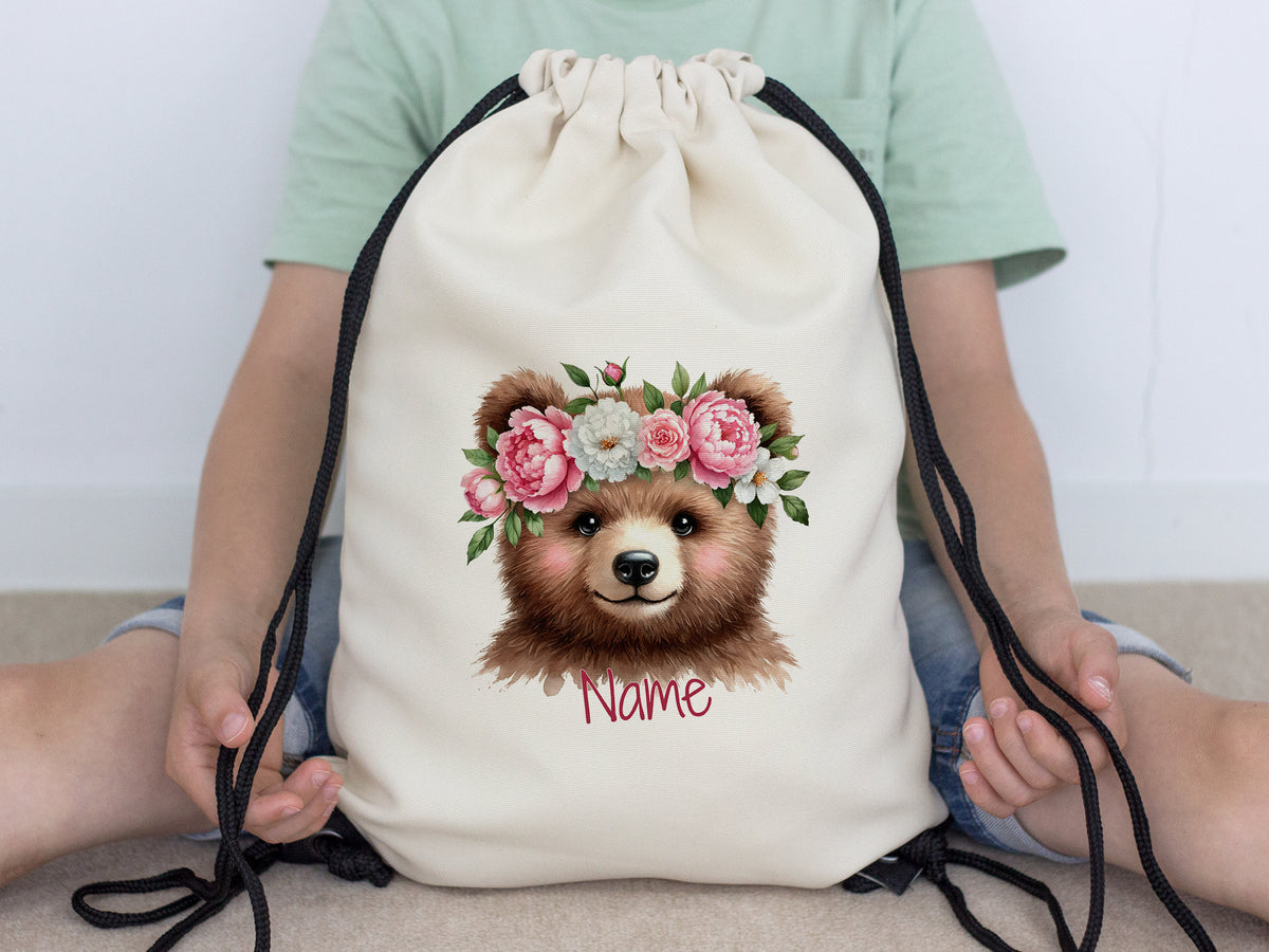Beige Turnbeutel mit Bärenmotiv und Blumenkranz.