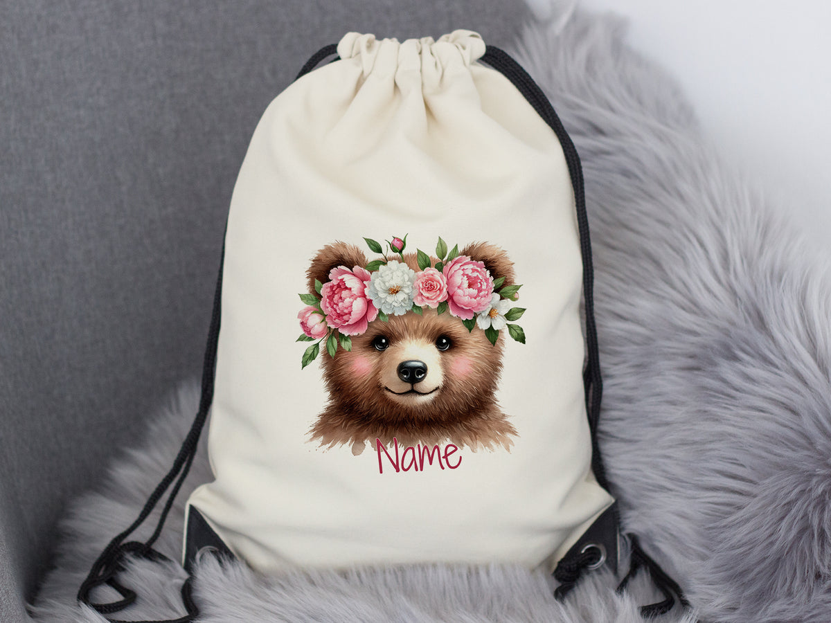 Beige Turnbeutel mit Bärenkopf und Blumenkranz.