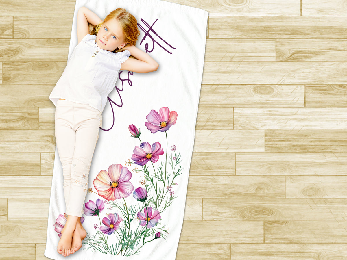 Mädchen auf Handtuch mit bunten Blumenmotiven.
