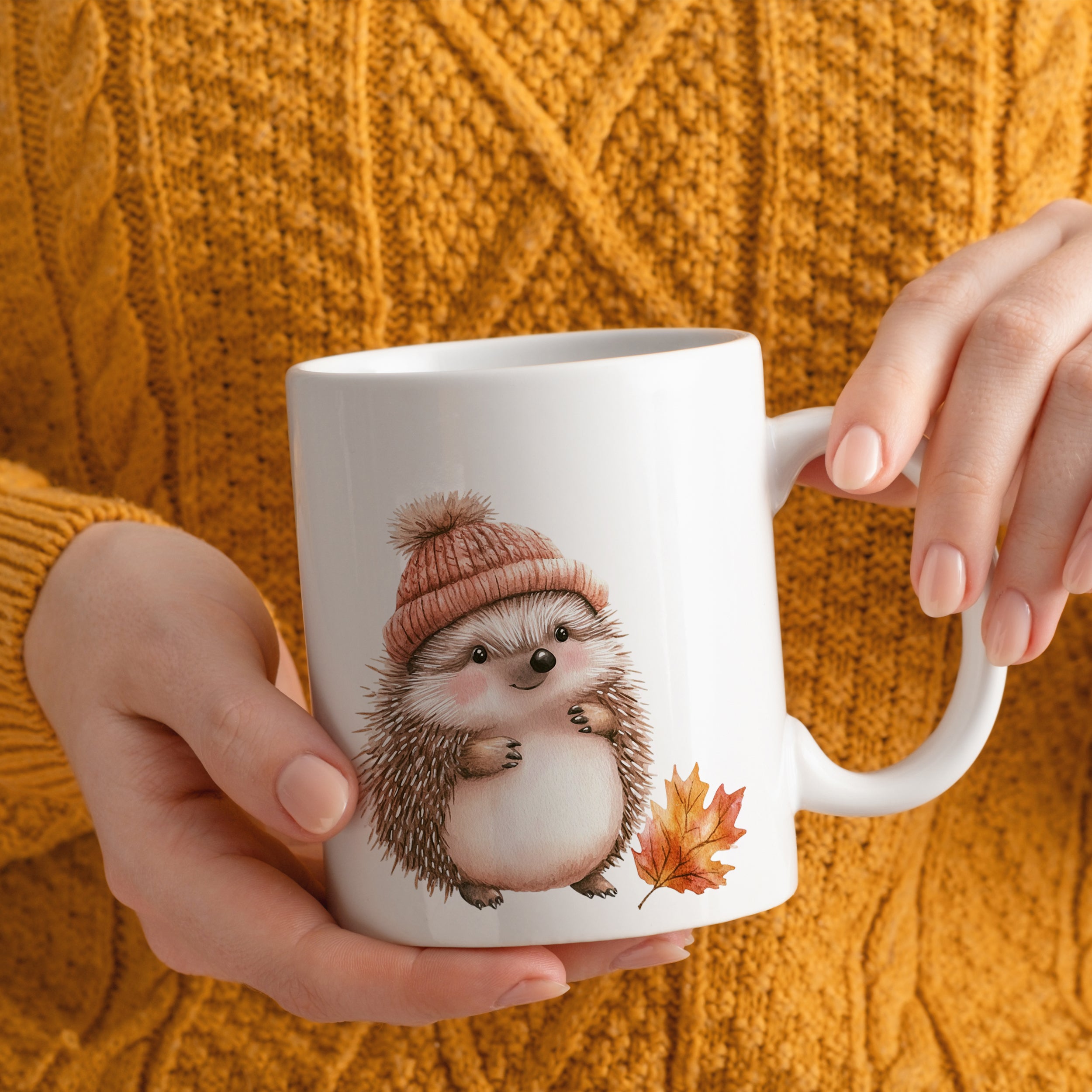 Weißer Becher mit Igel-Motiv und orangefarbener Mütze.