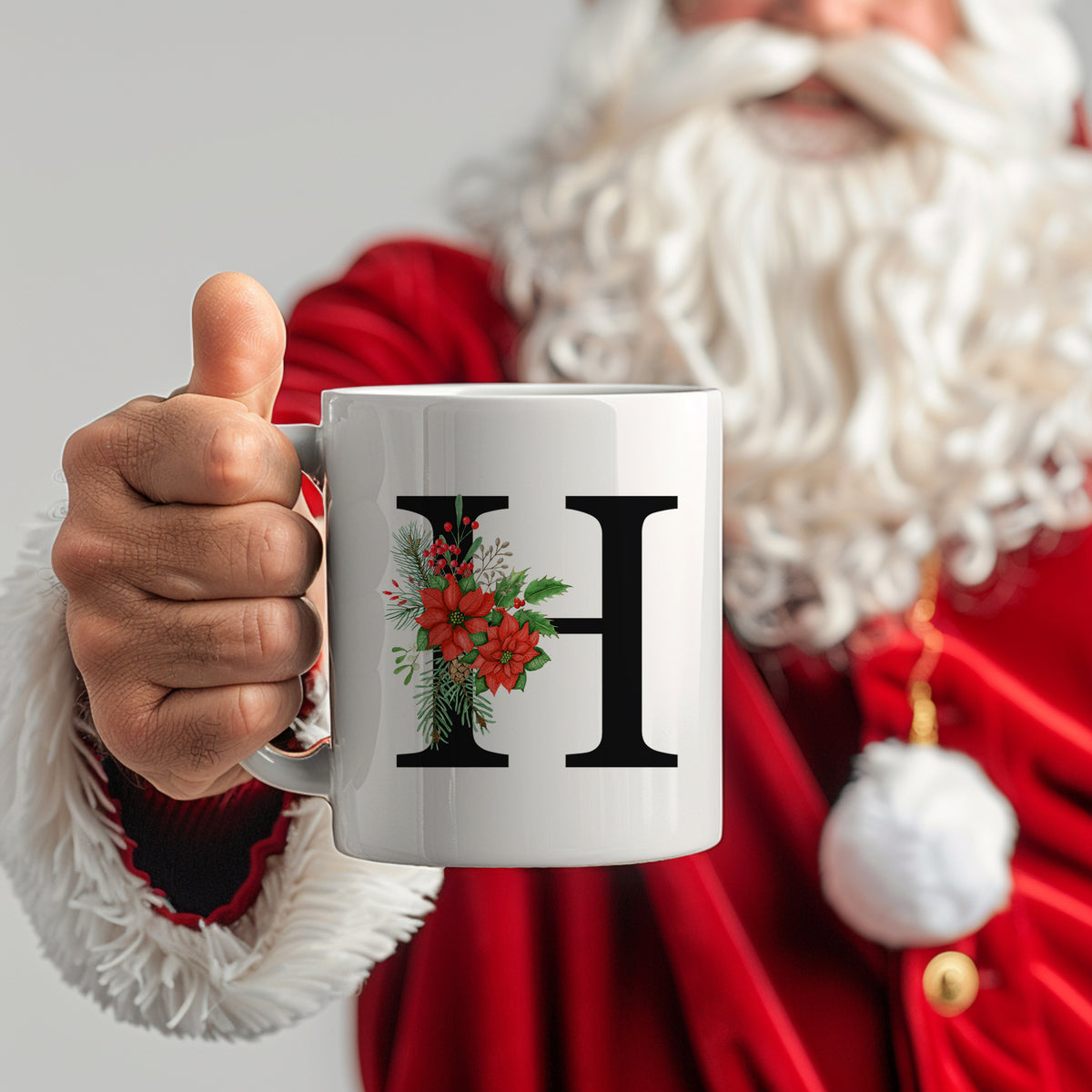 Weißer Becher mit schwarzem "H" und Weihnachtsdekor.