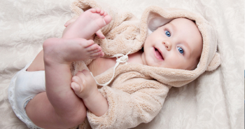 Baby in beigem Bärenanzug, fröhlich und spielerisch.