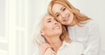 Zwei Frauen umarmen sich, eine mit grauen, die andere mit blonden Haaren.