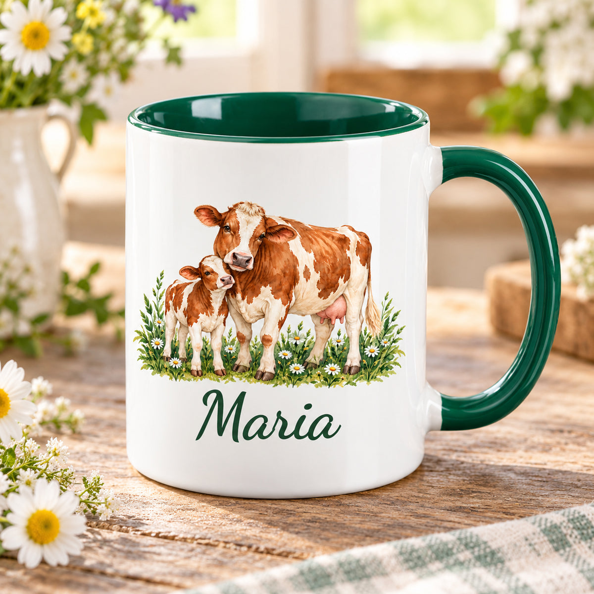 Kuh-Tasse mit braun-weißer Kuh und Kälbchen zwischen Wiesenblumen und Wunschname auf einem Holztisch mit Wiesenblumen