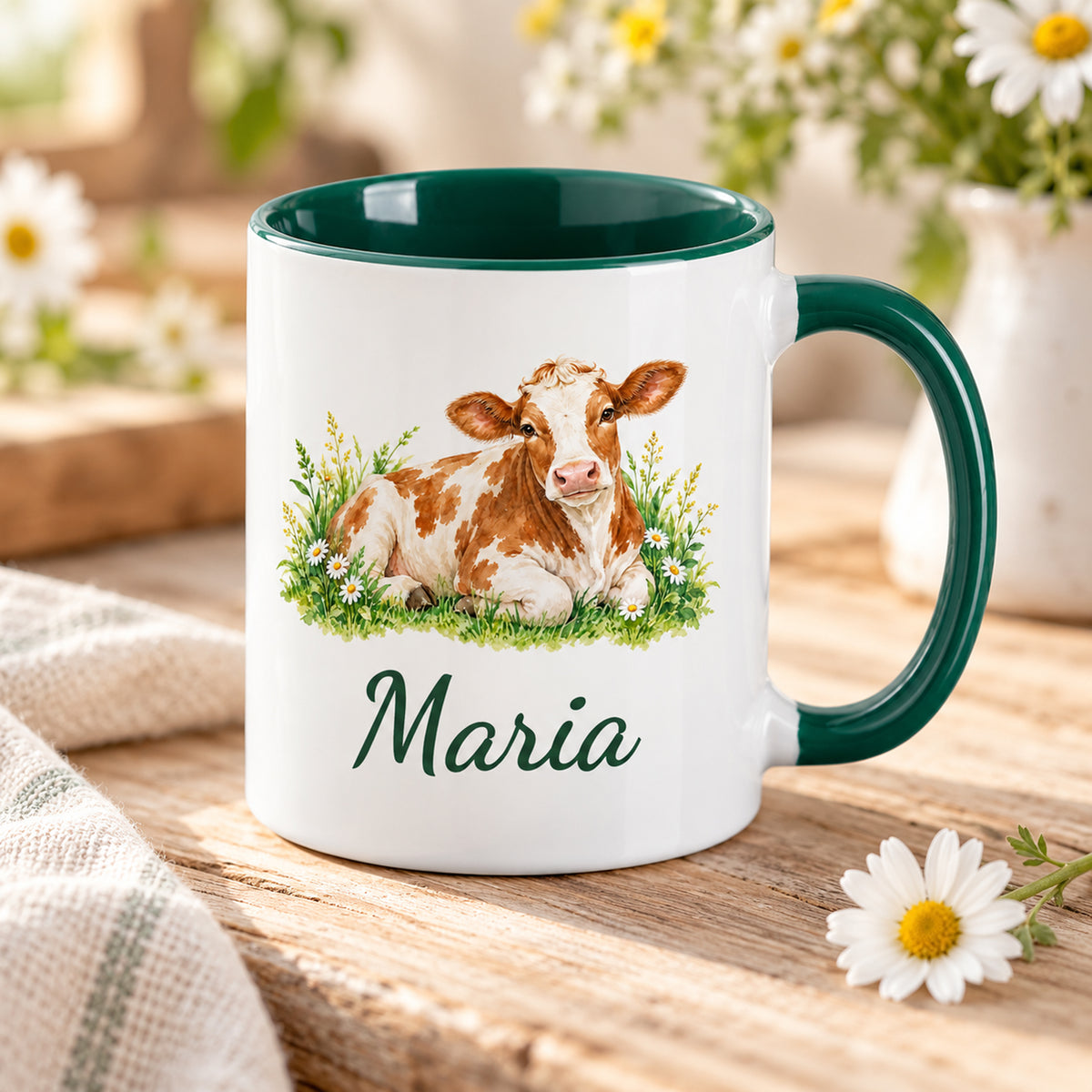 Kuh-Tasse mit ruhender braun-weißer Kuh mit Gänseblümchen und Wunschname in Schrägansicht mit sichtbarem dunkelgrünem Innenraum