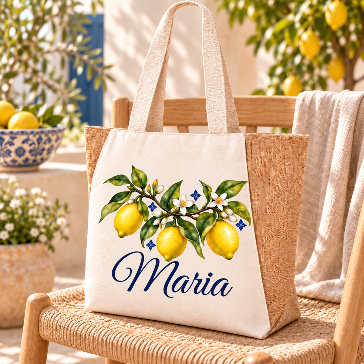 Naturfarbener Shopper mit drei Zitronen und Wunschname auf einem geflochtenen Holzstuhl auf einer sonnigen Terrasse.