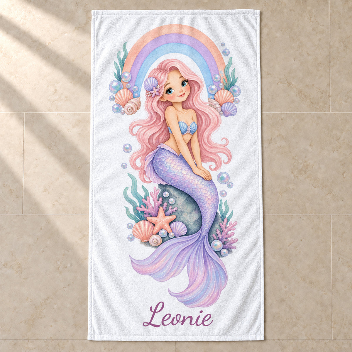 Personalisiertes Meerjungfrauen-Handtuch Regenbogenbucht mit Name Leonie, im Badezimmer aufgehängt.