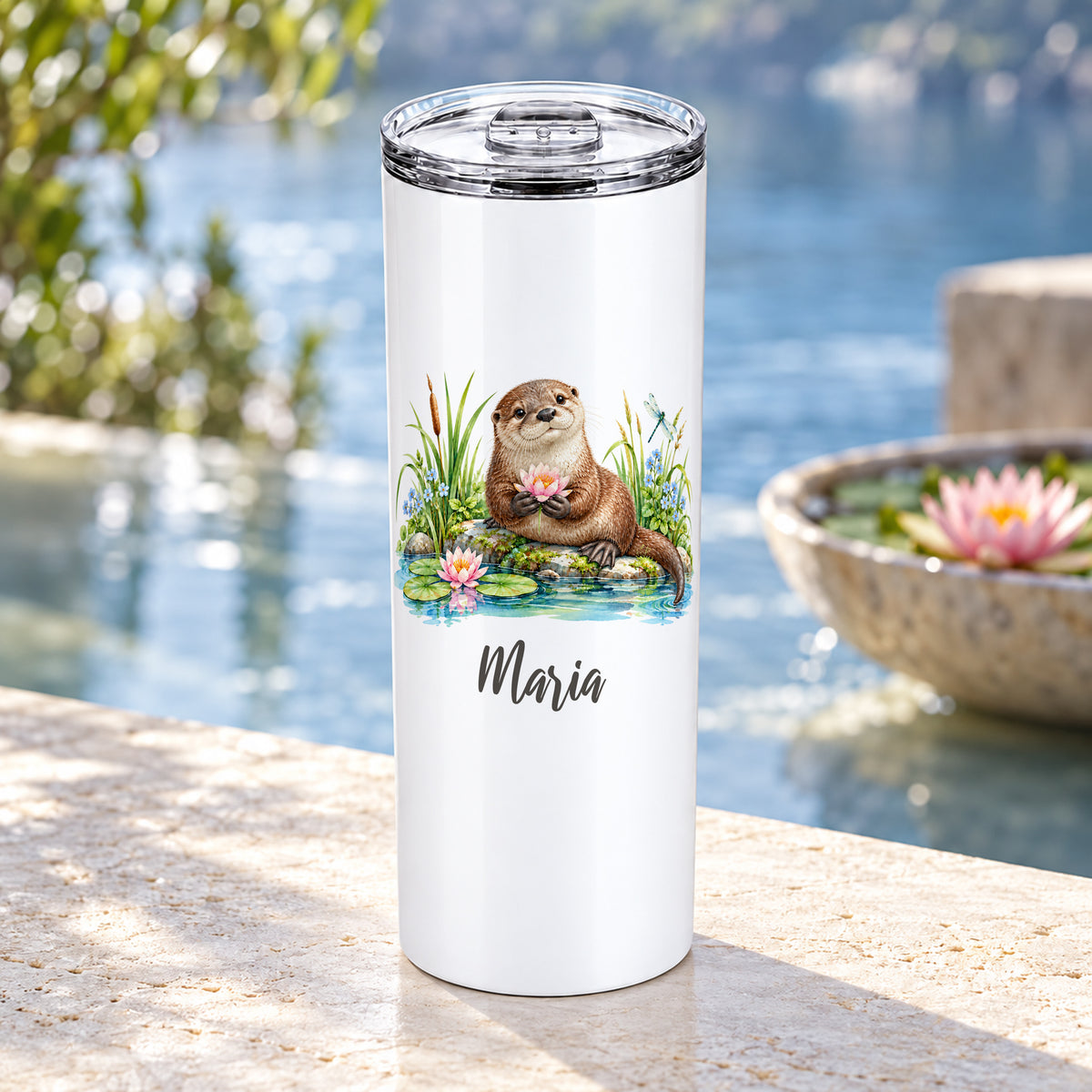 Weißer Thermobecher mit Otter-Aquarellmotiv und Wunschname an einem Gartenteich mit Seerosen.