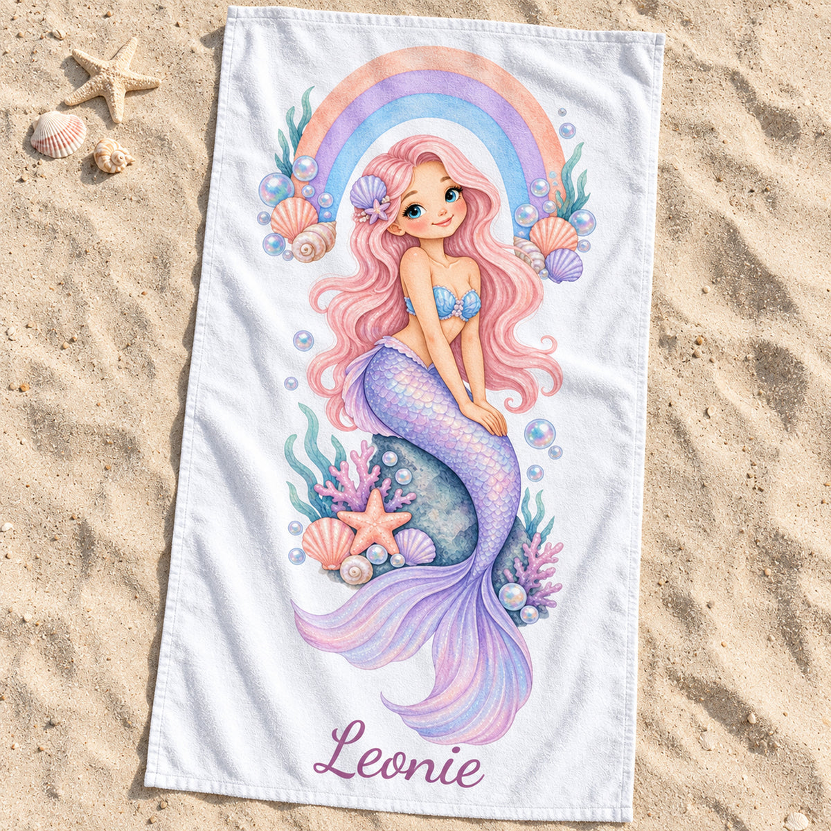 Handtuch mit Meerjungfrauenmotiv Regenbogenbucht und Beispielname Leonie auf Sand am Strand.