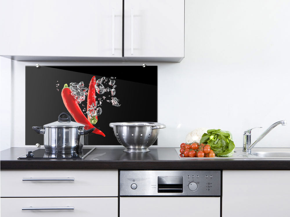 Rote Chilischoten spritzen in Wasser vor schwarzem Hintergrund.