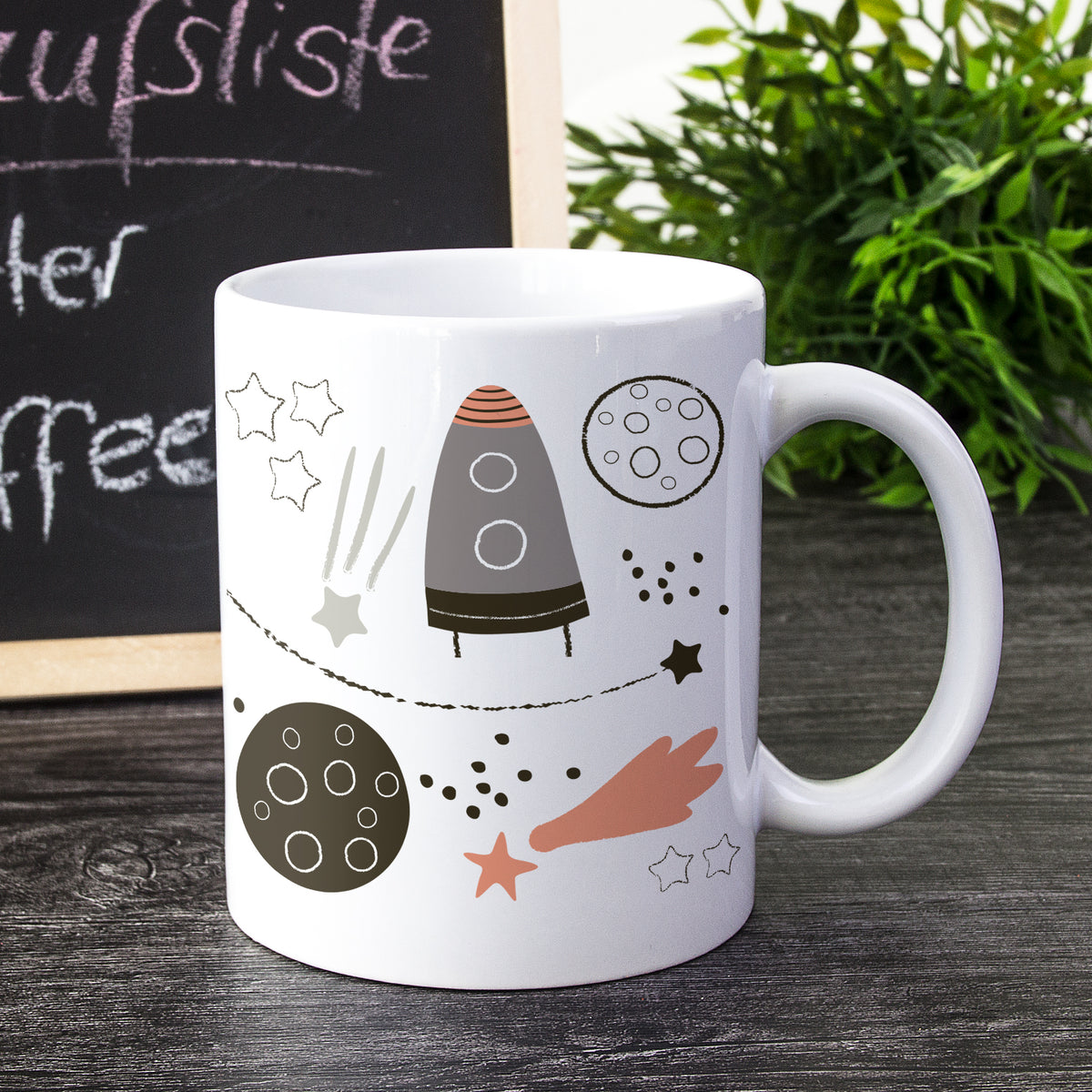 Weißer Kaffeebecher mit Rakete und Planeten-Motiv.