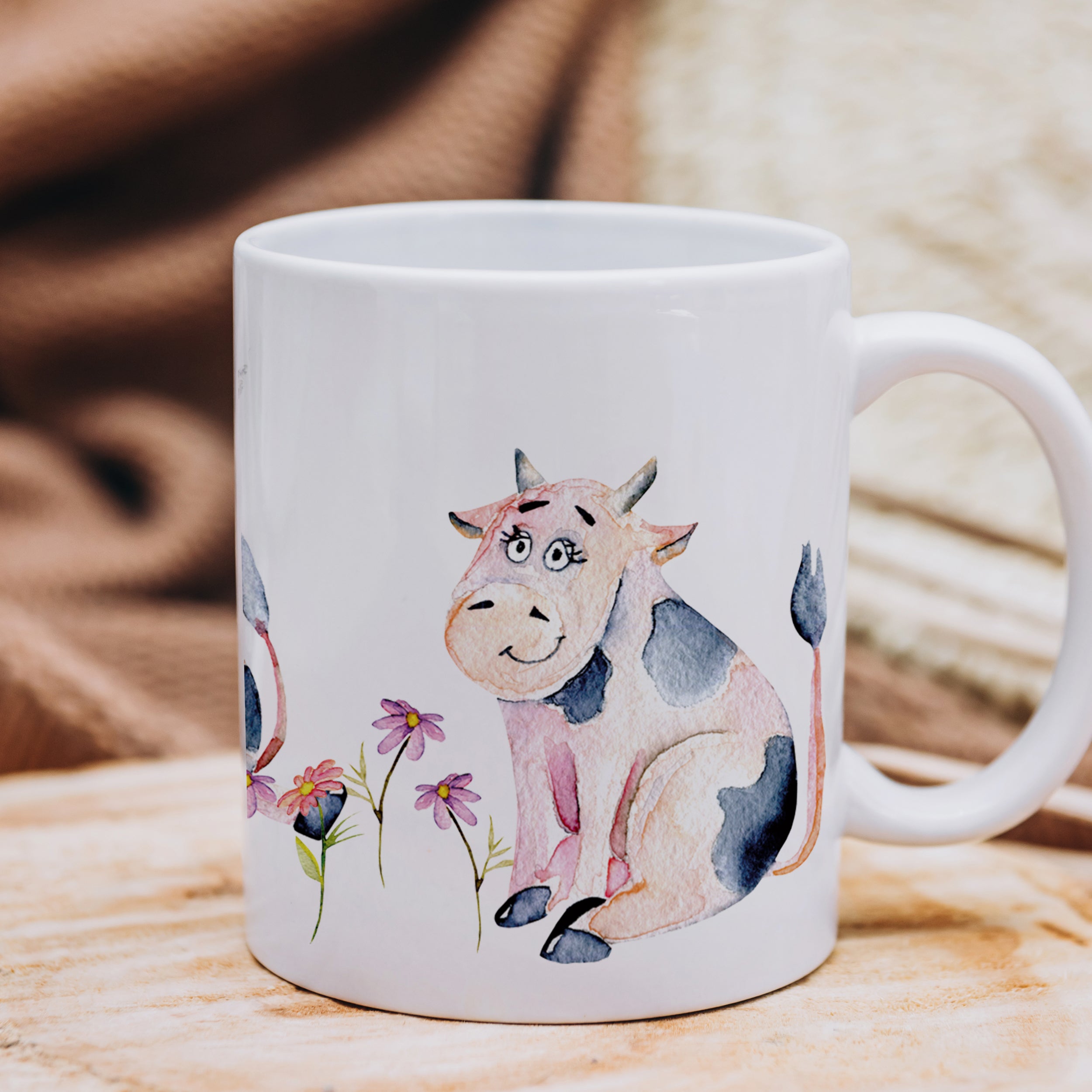 Tasse mit niedlicher Kuh-Illustration und bunten Blumen.