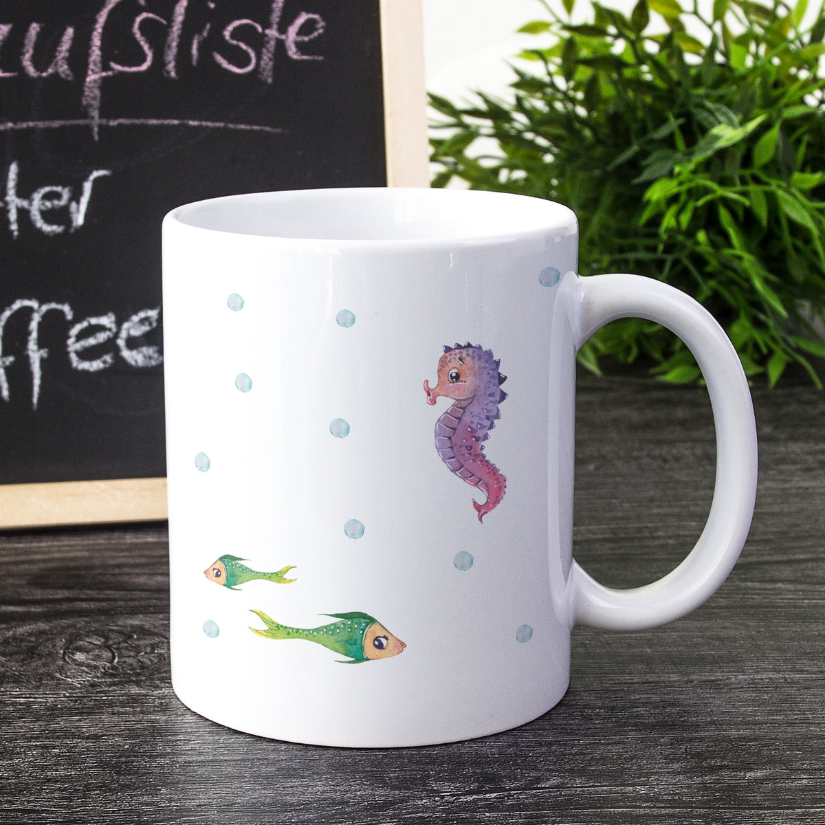 Weißer Becher mit Seepferdchen und bunten Fischen.