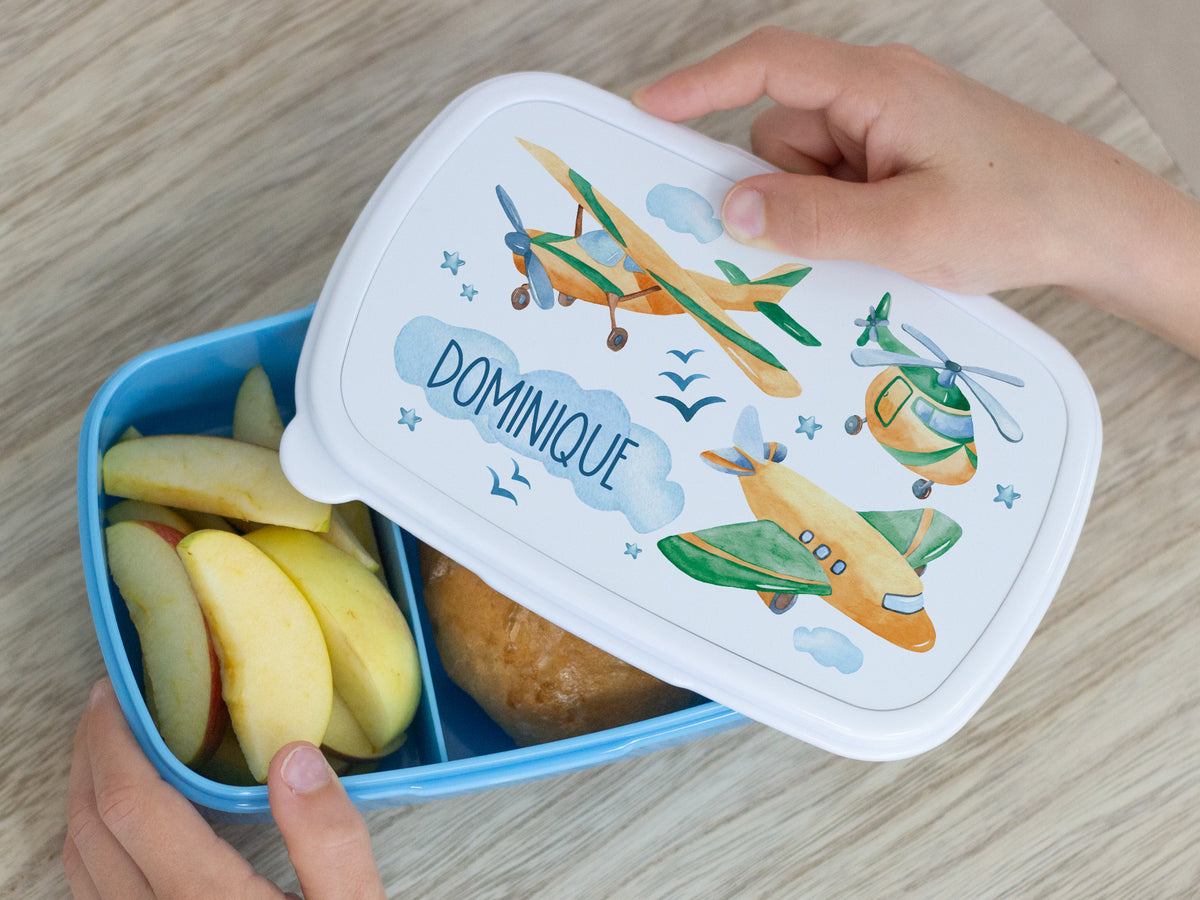 Bunte Brotdose mit Flugzeugen, Äpfeln und Brötchen.