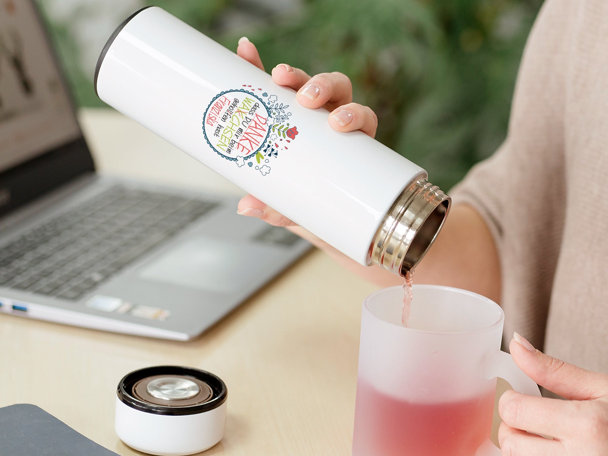 Weiße Thermosflasche mit buntem Aufdruck, Tee wird eingeschenkt.