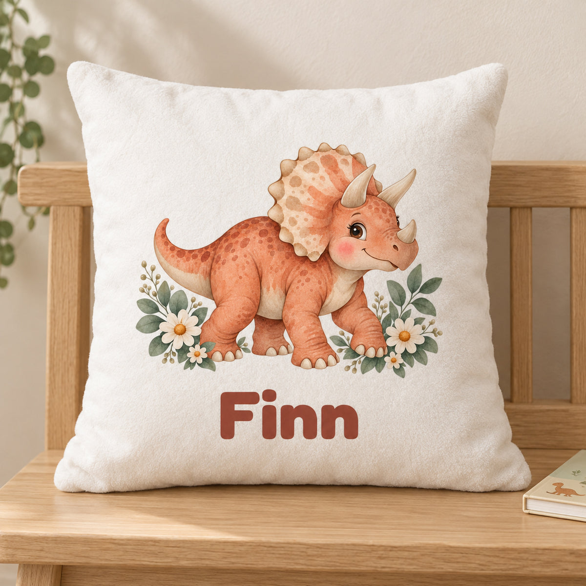 Personalisierter Dino-Kissenbezug: Triceratops mit Blumen, Beispielname Finn – Gedruckte Vorderseite auf Holzstuhl