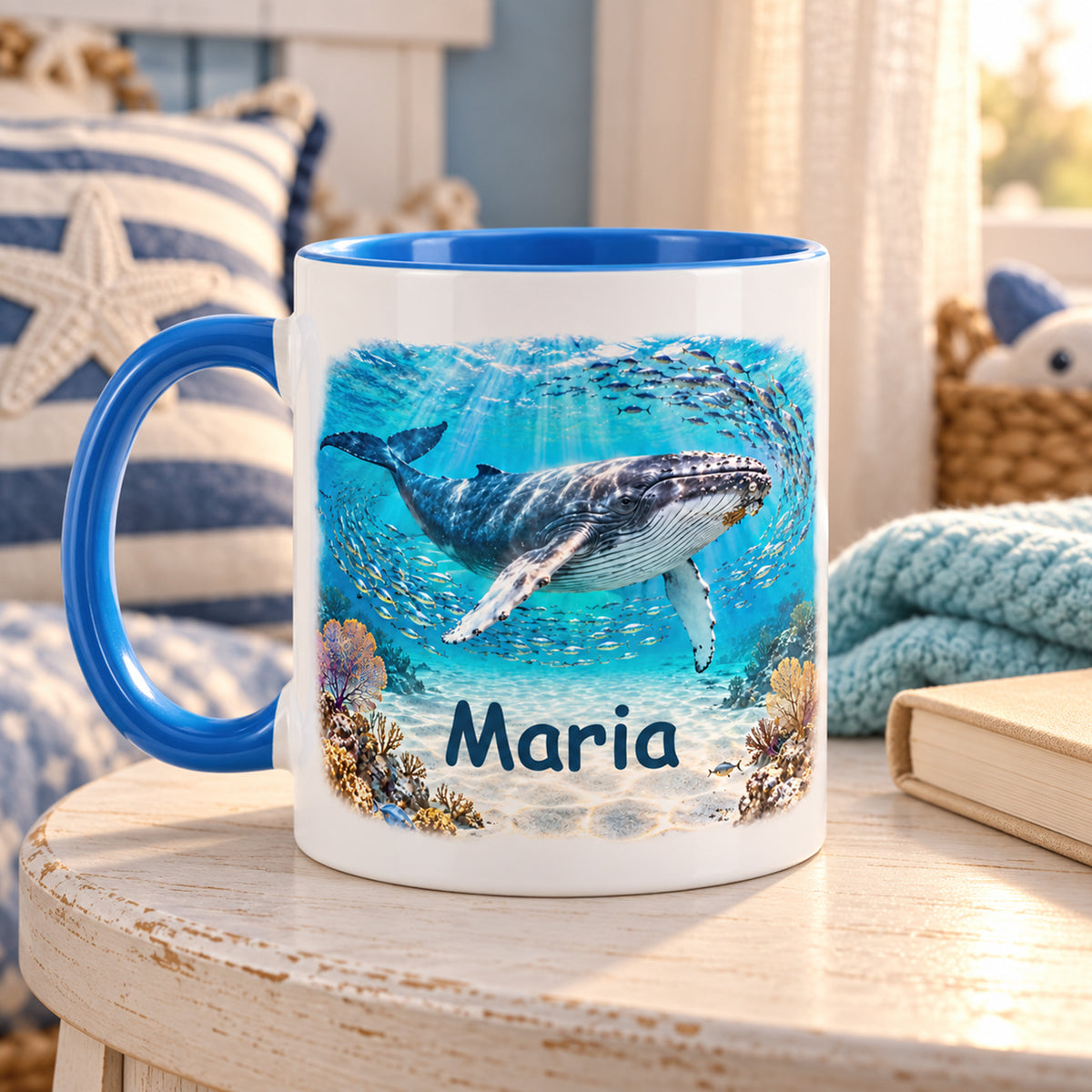 Wal-Tasse mit Fischschwarm und Name Maria auf einem Holztisch an einer Sofaecke mit Buch