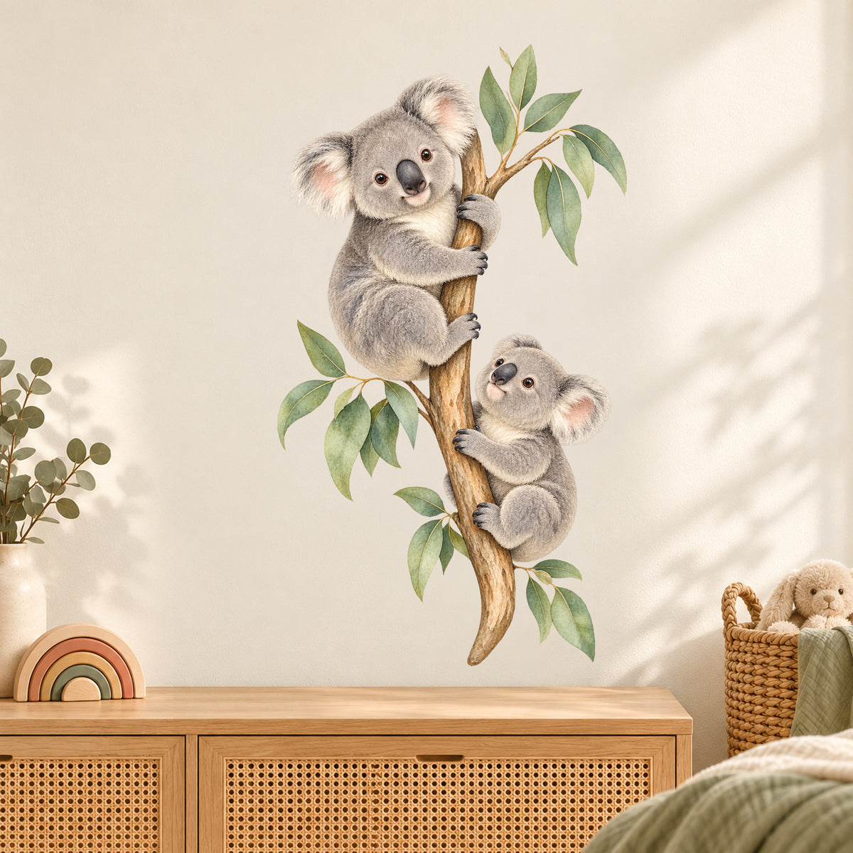 Koala-Wandtattoo Kletterfreunde an einer cremefarbenen Kinderzimmerwand über einer Holzkommode mit Geflechtfronten.
