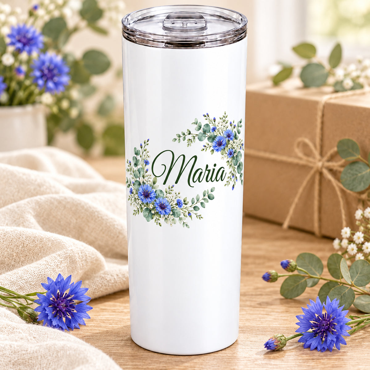 Weißer Thermobecher mit Motiv Kornblumentraum, Blumenranke und Name Wunschname auf einem dekorierten Geschenktisch.