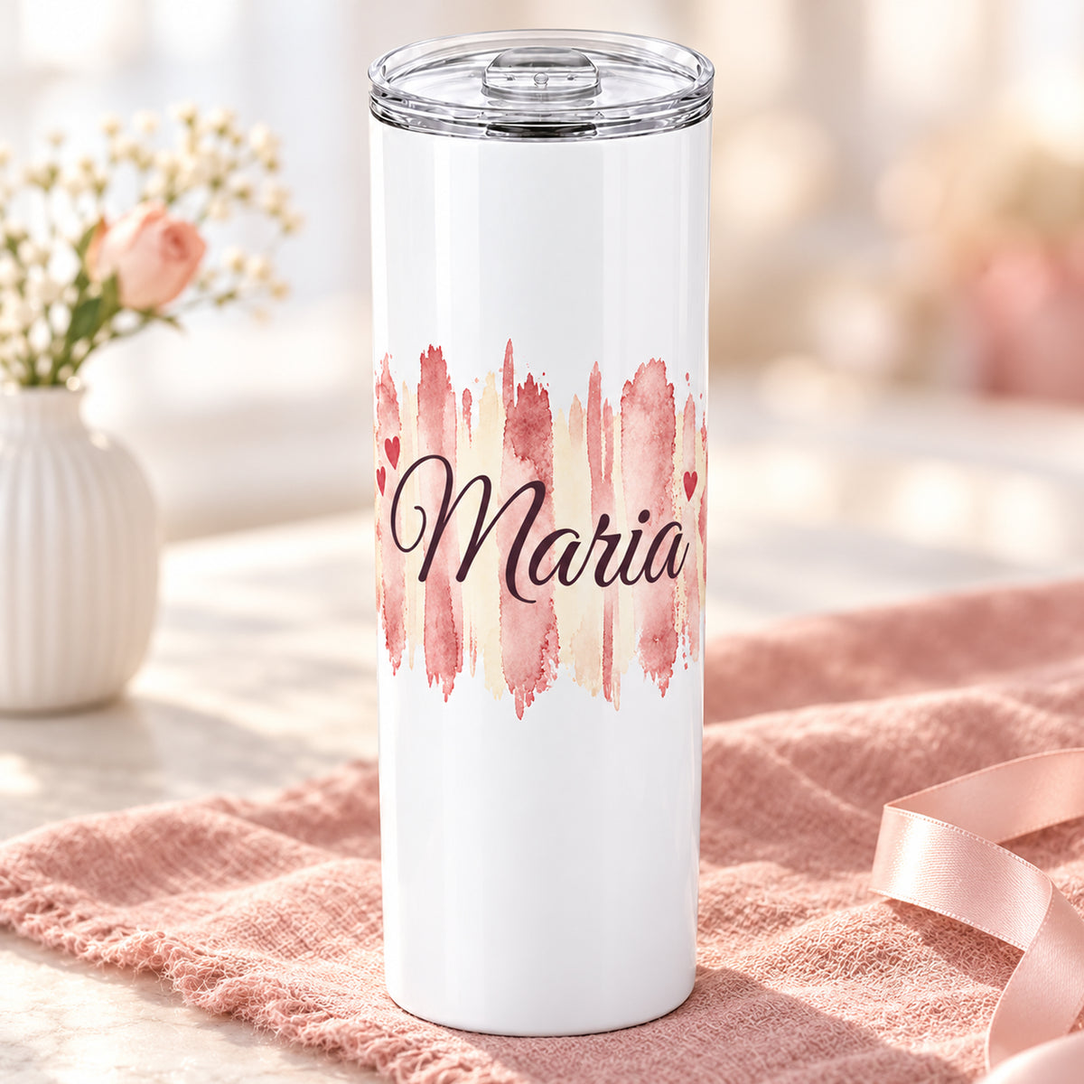 Weißer Thermobecher mit Motiv Herzensrosa, personalisiertem Namen auf einem dekorierten Geschenktisch.