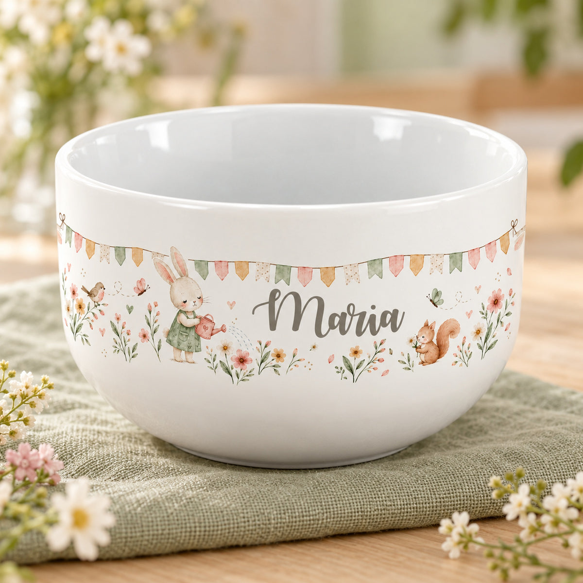 Personalisierte Keramik-Müslischale mit Häschen mit Gießkanne, Vogel und Eichhörnchen und Blumen auf einem hellen Tisch.