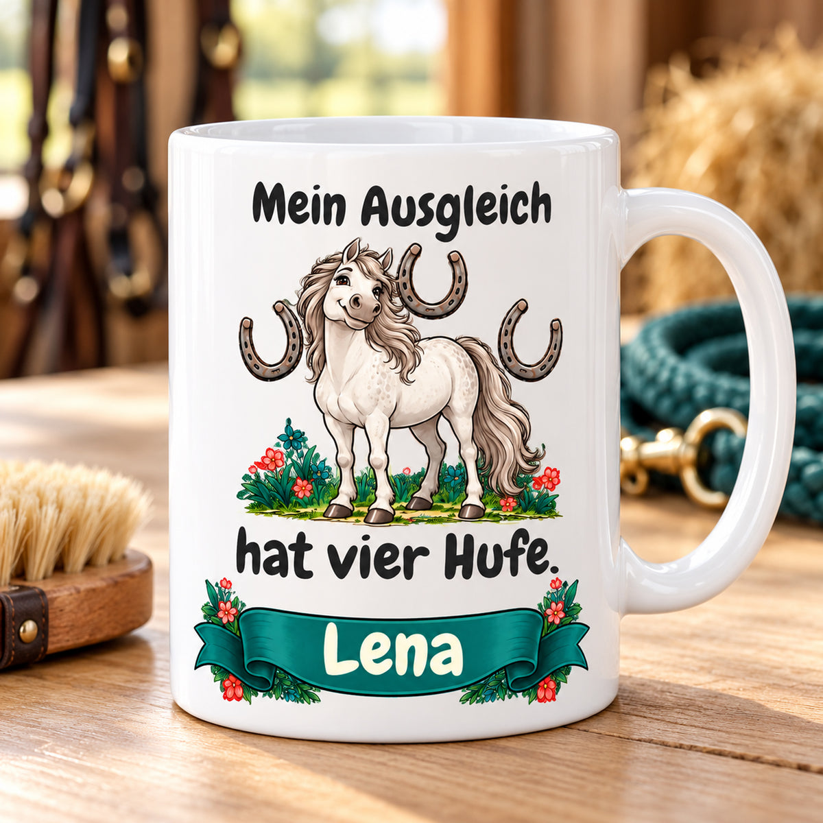 Weiße Pferdetasse mit Namen, Schimmel und Hufeisen und Spruch „Mein Ausgleich hat vier Hufe.“, auf heller Ablage.