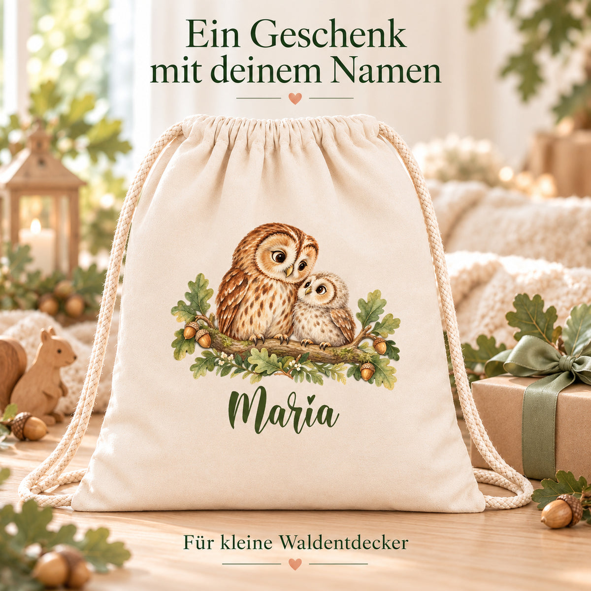 Personalisierter Turnbeutel mit Eule und Jungvogel neben einem verpackten Geschenk und Walddekoration