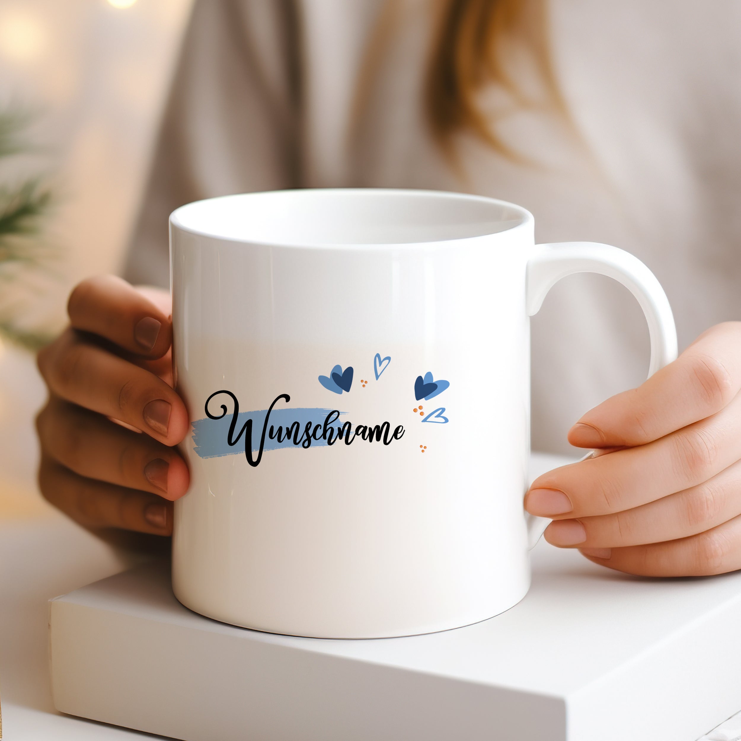 Weiße Tasse mit Schriftzug "Wunschname" und blauen Herzen.